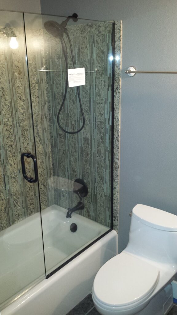 a shower door and panel on top of a tub, the panel is attached to the wall and the tub using a metal channel, which can be glued down to avoid damaging the fiberglass tub