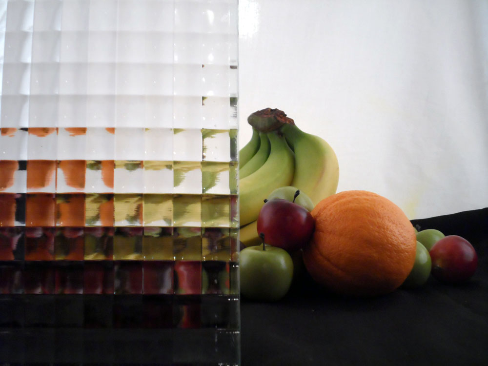 a glass display with some fruit half covered by glass, the glass has many square bumps in a grid pattern, the fruit is fairly visible