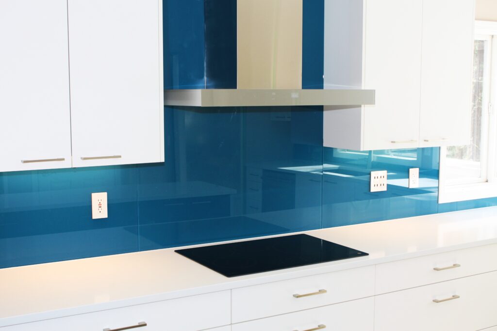 a kitchen counter and stove with blue backpainted glass backsplash