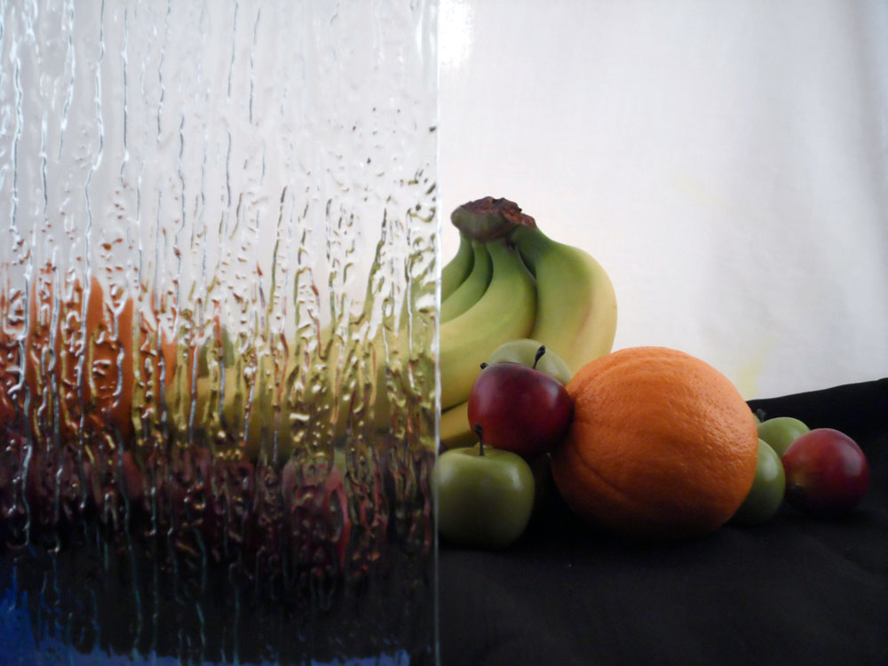 a glass display with some fruit half covered by glass, the glass is molded with streaks in it to look like rain, the fruit is visible but blurry